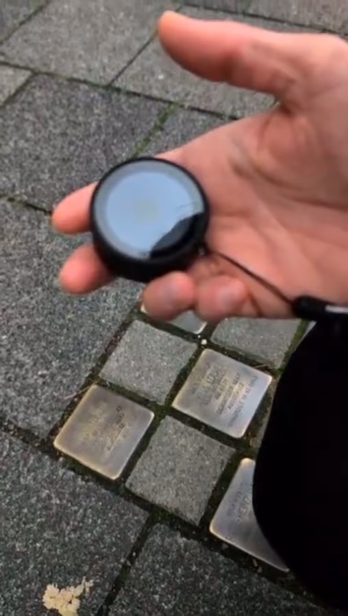 Eine Hand hält den Dialogstein über vier Stolpersteinen im Pflaster